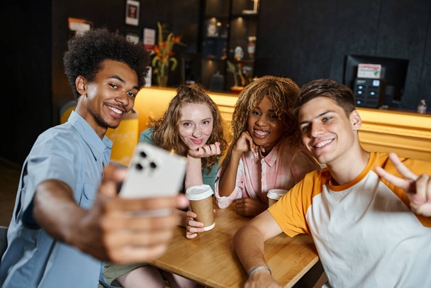 fröhlicher afrikanisch-amerikanischer Mann macht Selfie mit stilvollen multiethnischen Freunden in der Lounge des Hostels - Foto, Bild
