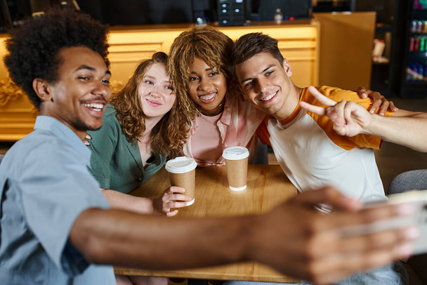 Heyecanlı Afrikalı Amerikalı öğrenci mutlu çok kültürlü arkadaşlarıyla oteldeki kafede selfie çekiyor. - Fotoğraf, Görsel