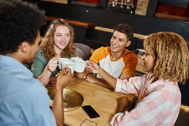 zorgeloze multi-etnische studenten klinkende koffiekopjes in lobby cafe van jeugdherberg, reizigers - Foto, afbeelding