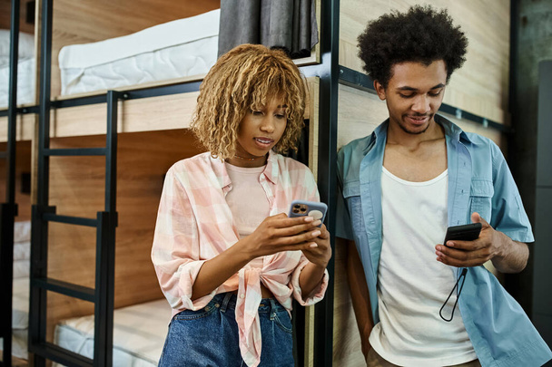 стильні афроамериканські сусіди в кімнатах використовують смартфони біля двоповерхових ліжок в затишному студентському гуртожитку - Фото, зображення