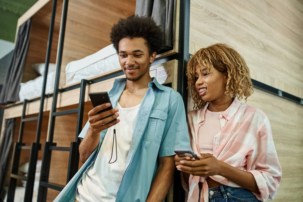 mosolygós afro-amerikai férfi böngészés internet okostelefon közelében barátnője a diákok hostel - Fotó, kép
