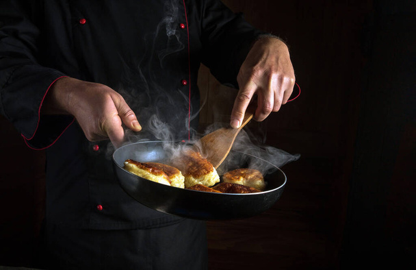 Egy profi séf tésztafánkot süt egy serpenyőben. Éttermi menü vagy recept helye sötét háttérrel. - Fotó, kép