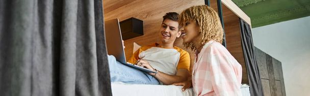 smiling african american woman near friend networking on laptop on double-decker bed, banner - Photo, Image