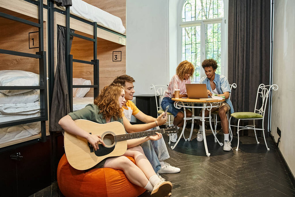 monikulttuurinen opiskelijoiden kitara ja kannettava huone nykyajan retkeilymaja, matkustajat - Valokuva, kuva