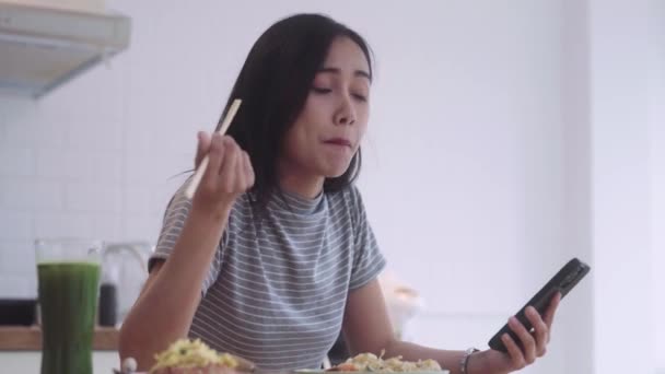 χαρούμενη Ασιάτισσα γυναίκα που έχει ασιατικά noodles food pad thai κρατώντας chopsticks για μεσημεριανό κατά τη διάρκεια του διαλείμματος και πληκτρολογώντας στο smartphone της  - Πλάνα, βίντεο