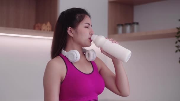 Здоровая спортивная молодая азиатка в спортивной одежде держит и пьет чистое молоко или сыворотку здорового питания на кухне дома, здравоохранение и потеря веса концепции. Высококачественные 4k кадры - Кадры, видео