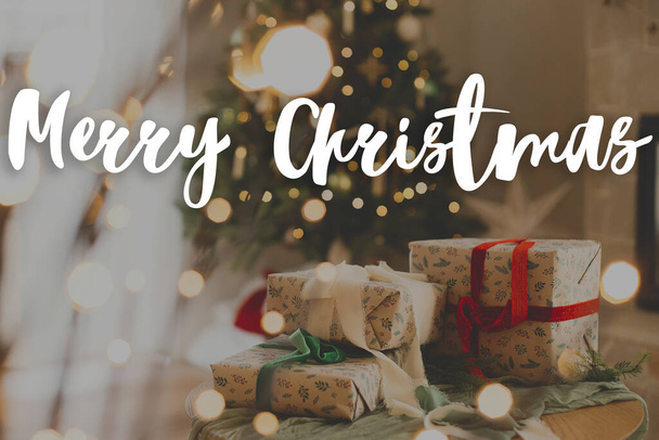 Noel ağacının ve şenlikli ışıkların arka planında kurdeleyle paketlenmiş şık Noel hediyeleriyle ilgili mutlu Noeller metni. İyi tatiller! Sezonun tebrik kartı. El yazısı işareti - Fotoğraf, Görsel