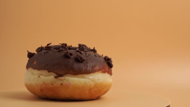 A donut covered in chocolate with chocolate chips rotates on an orange background. Sweet bun close-up. - Footage, Video