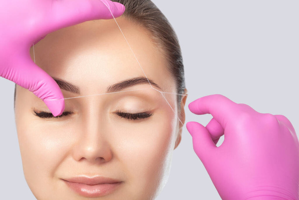 The make-up artist plucks eyebrows with a thread close-up. Women's cosmetology in the beauty salon. - Photo, Image