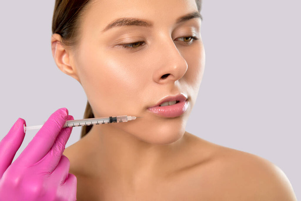 Woman with beautiful clean skin. Cosmetologist does injections for lips augmentation and anti wrinkle in the nasolabial folds of a beautiful woman. Women's cosmetology in the beauty salon. - Photo, Image
