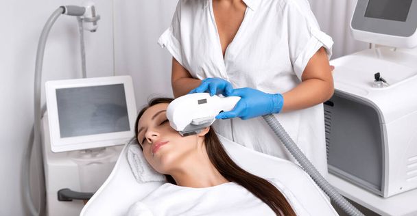 Epilation Haarentfernung auf dem Gesicht einer Frau. Kosmetikerin bei der Laserverjüngung am Kinn in einem Schönheitssalon. Gesichtspflege. Hardware IPL Kosmetologie - Foto, Bild