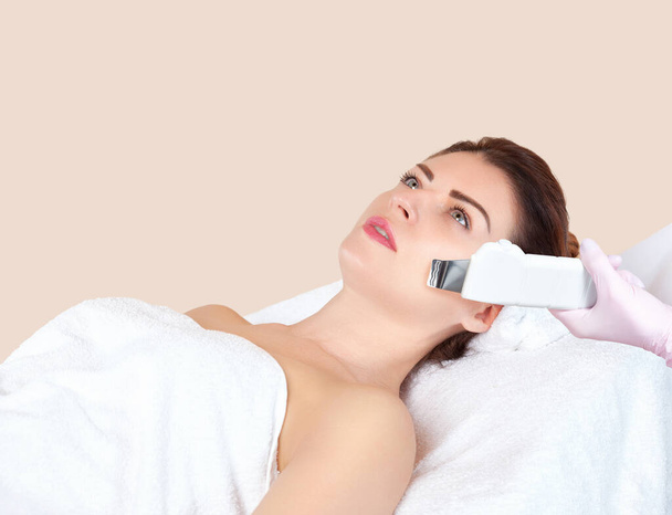 Ο κοσμητολόγος κάνει την υπερηχογραφική διαδικασία καθαρισμού του δέρματος του προσώπου μιας γυναίκας σε ένα σαλόνι ομορφιάς. Καλλυντικά και επαγγελματική περιποίηση του δέρματος. - Φωτογραφία, εικόνα