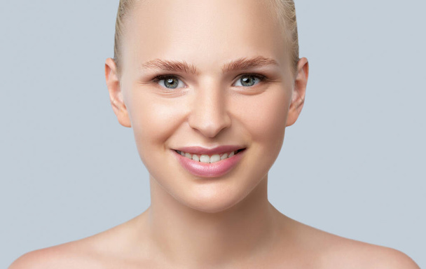 Πορτρέτο μιας όμορφης χαμογελαστής ξανθιάς γυναίκας με γυμνούς ώμους, με μπλε μάτια, παχουλά χείλη, καθαρό δέρμα και φρέσκο μακιγιάζ. Αισθητική κοσμετολογία, θεραπεία μαλλιών και μακιγιάζ έννοια. - Φωτογραφία, εικόνα