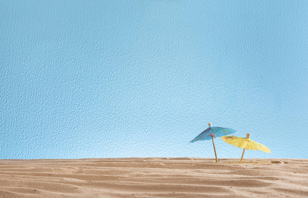 коктейльные зонтики в песке на синем фоне, абстрактная текстура для дизайна, копирайтинг, концепция летних каникул - Фото, изображение
