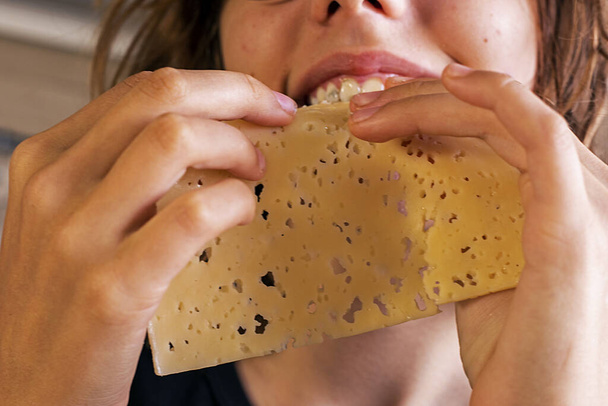 manos de una chica joven tomar queso duro, cortado en rodajas finas, y comerlo - Foto, Imagen