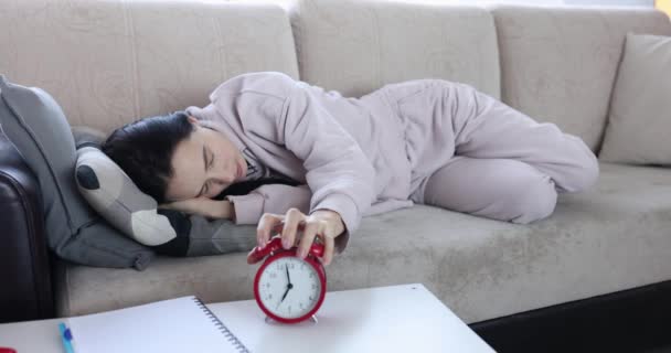 Nukkuva laiska nainen makaa sohvalla ja sammuttaa soivan herätyskellon. Päiväaikainen uneliaisuus ja masennus - Materiaali, video