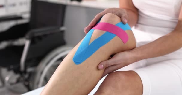 Woman holding her sore knee with hand with kinesio tapes 4k movie slow motion. Kinesiotherapy rehabilitation after trauma concept - Footage, Video