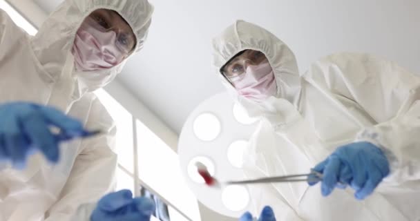 Kirurgit suojapuvuissa ja suojalasit suorittaa leikkauksen tarttuva potilaan alhaalta näkymä 4k elokuva hidastettuna. Kirurginen hoito potilaille kovettuma19 käsite - Materiaali, video