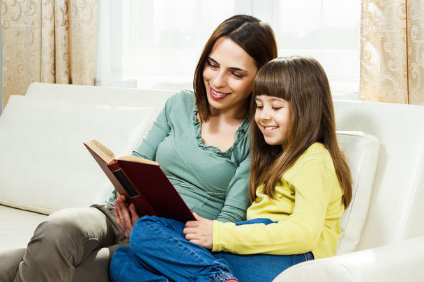 Mother and daughter sitting on sofa and reading a book - Foto, Imagem