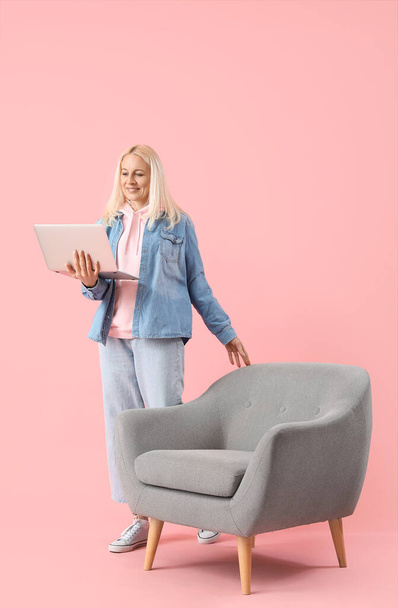 Зрелая женщина-программист работает с ноутбуком на розовом фоне - Фото, изображение