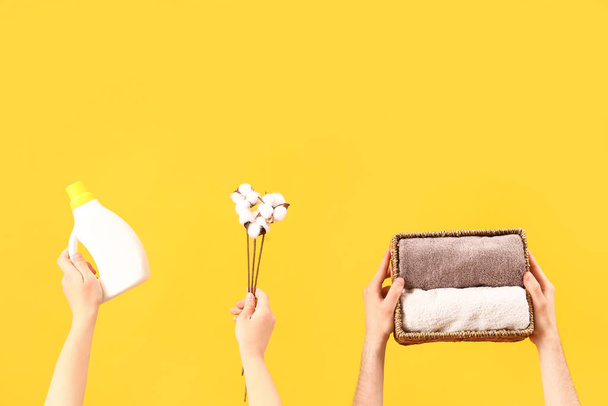 People with laundry detergent, cotton flowers and clean towels on yellow background - Photo, Image