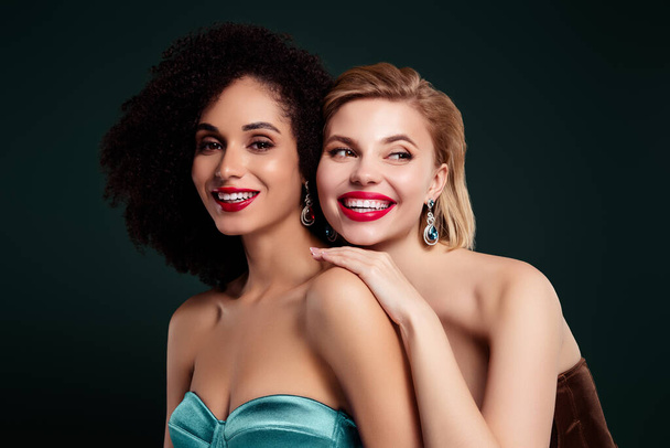 Photo of joyful pretty girls smiling touch shoulders look over dark green color empty space background. - Photo, image