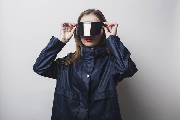 Mladá žena nosí brýle virtuální reality, v modré bundě na světlém pozadí. - Fotografie, Obrázek