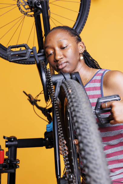 Αφιερωμένο μαύρο γυναίκα αναλύει στενά ποδήλατο αλυσίδα διαμονή για να διατηρήσει την αποδοτικότητα του κύκλου. Αφροαμερικάνα ποδηλάτισσα με έμφαση στην επισκευή αλυσίδων τροχών ποδηλάτων με εξειδικευμένο εξοπλισμό. - Φωτογραφία, εικόνα