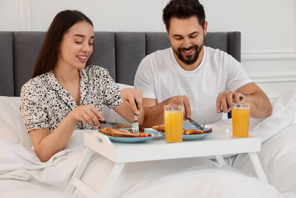 Happy couple having breakfast on bed at home - 写真・画像