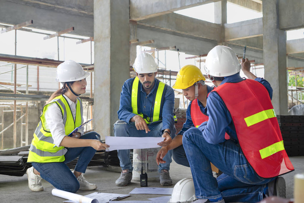 Mérnöki vagy építészeti munka koncepció, mérnökök munkatársak visel sisak és biztonsági mellény megvitatják tervrajz a padlón - Fotó, kép