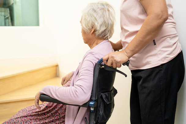 Опекун помочь азиатской или пожилой пожилой женщины сидя инвалидной коляски поддержки вверх по лестнице в доме. - Фото, изображение