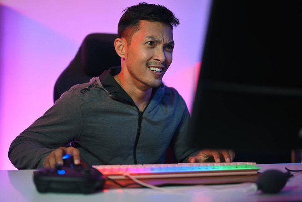 Радісний гравець грає в відеоігри онлайн вдома з барвистими неоновими вогнями - Фото, зображення
