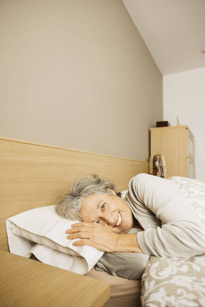 Портрет улыбающейся пожилой женщины в постели рано утром. - Фото, изображение