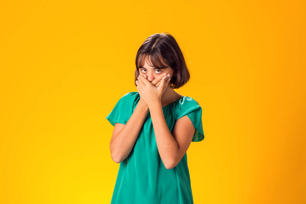 Налякана дівчина покрила рот руками над жовтим тлом - Фото, зображення
