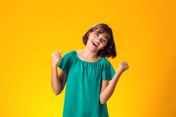 Χαμογελαστό κορίτσι που δείχνει επιτυχία σε κίτρινο φόντο. Αντίληψη τύχης - Φωτογραφία, εικόνα