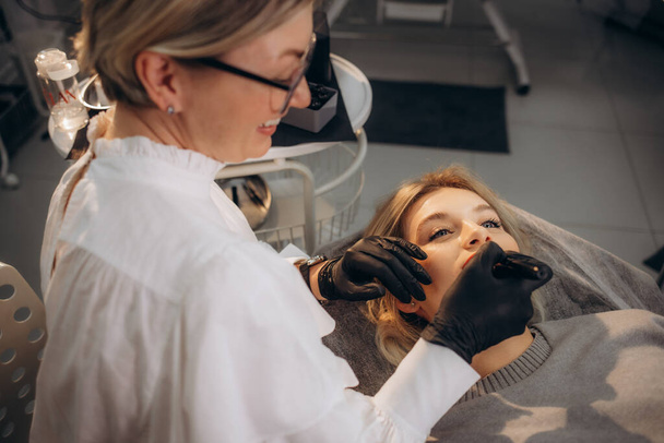 El cosmetólogo hace maquillaje permanente en la cara de una mujer. Especialista aplica un tatuaje en los labios del paciente de cerca. Foto de alta calidad - Foto, imagen