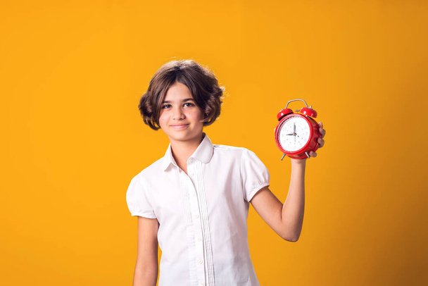 Девочка держит будильник в руке. Понятие образования, школа, сроки, время на учебу - Фото, изображение