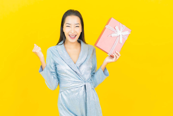 Porträt schöne junge asiatische Frau lächeln mit rotem Geschenkkarton auf gelbem Hintergrund - Foto, Bild