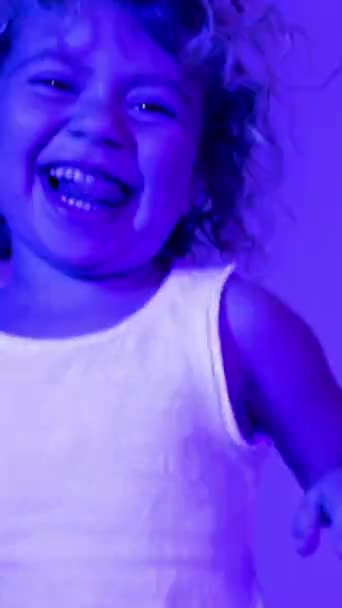 Una linda niña dj con auriculares con iluminación disco de colores en vertical - Imágenes, Vídeo