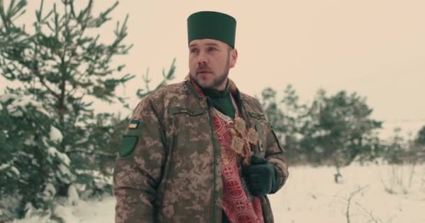 Μάγος με στρατιωτική στολή του ουκρανικού στρατού. Πορτραίτο ενός νεαρού ιερέα σε έναν χιονισμένο ανοιχτό χώρο. Πόλεμος της Ουκρανίας με τη Ρωσία. - Πλάνα, βίντεο