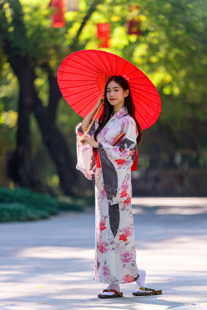 Une jeune femme portant un kimono traditionnel japonais ou un yukata tenant un parapluie est heureuse et joyeuse dans le parc. Robe d'été traditionnelle japonaise. - Photo, image