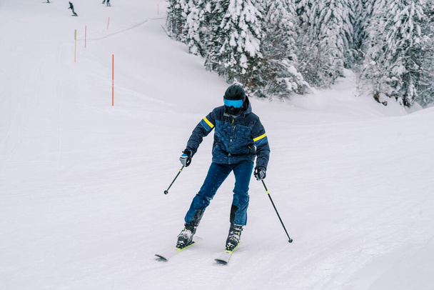 Skieur en équipement de ski, penché sur le côté, sur des skis le long d'une piste enneigée. Photo de haute qualité - Photo, image