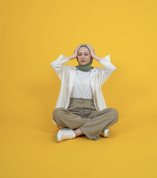 Mujer musulmana caucásica deprimida, estudio de cuerpo completo sentado retrato de mujer musulmana caucásica deprimida. Manteniendo la cabeza con las manos cerradas. Sufriendo dolor, dolor de cabeza. Concepto de vida. - Foto, Imagen