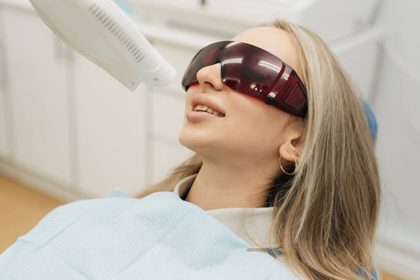 Dentes branqueamento procedimento com luz ultravioleta lâmpada UV. Retrato de close-up de uma paciente do sexo feminino no dentista na clínica - Foto, Imagem