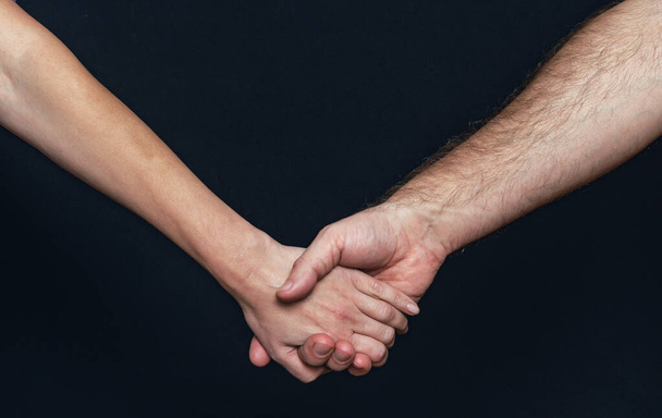 De hand van een vrouw houdt een man vast. Handjes vasthouden op een zwarte achtergrond - Foto, afbeelding