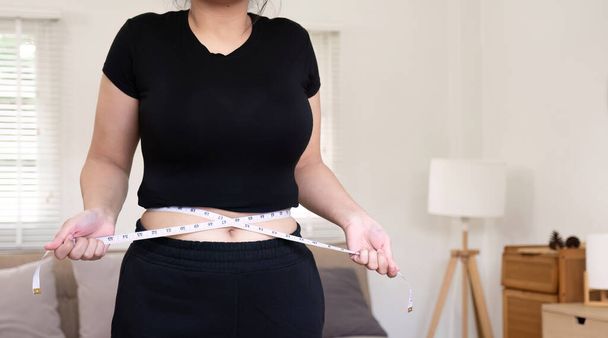 Buclatá žena používá měřicí pásku k měření břicha.. - Fotografie, Obrázek