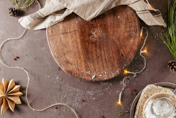 Planche à découper sur une table de cuisine avec décoration de Noël, sucre, étoiles de papier et branches de pin naturel sur fond sombre. Vue de dessus, composition de concept de maquette de vacances d'hiver - Photo, image