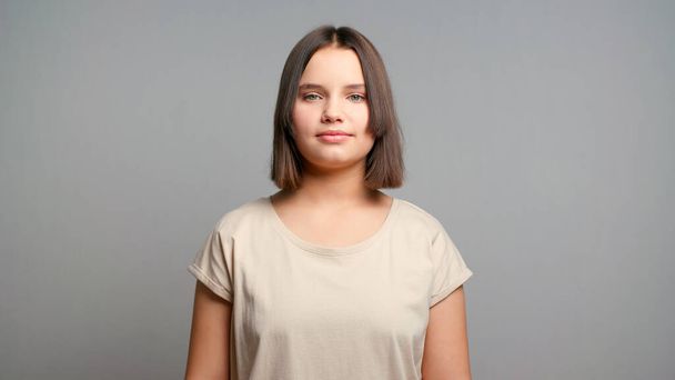 Портрет молодого латинського студентки-підлітка в бежевій футболці, посміхаючись ізольовано на сірому фоні. Копіювати простір. - Фото, зображення