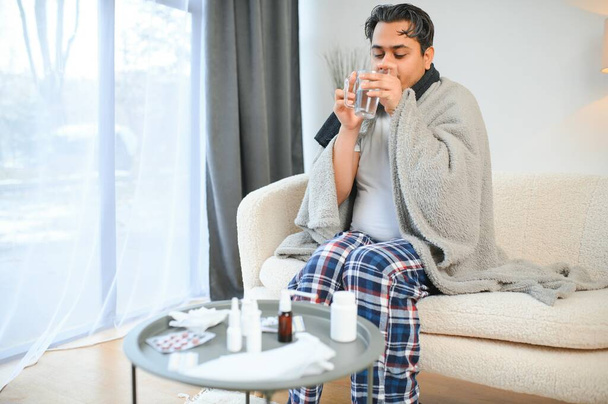 health, cold and people concept - sick young indian man in blanket having headache or fever at home. - Фото, изображение