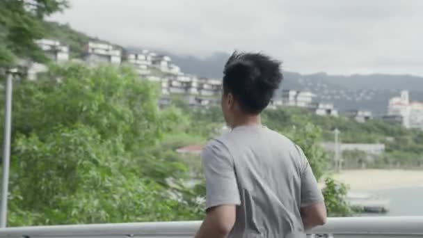 vista laterale di giovane asiatico uomo jogging running all'aperto in parco - Filmati, video